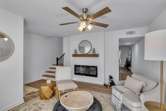 living area with a large fireplace, baseboards, visible vents, stairway, and wood finished floors