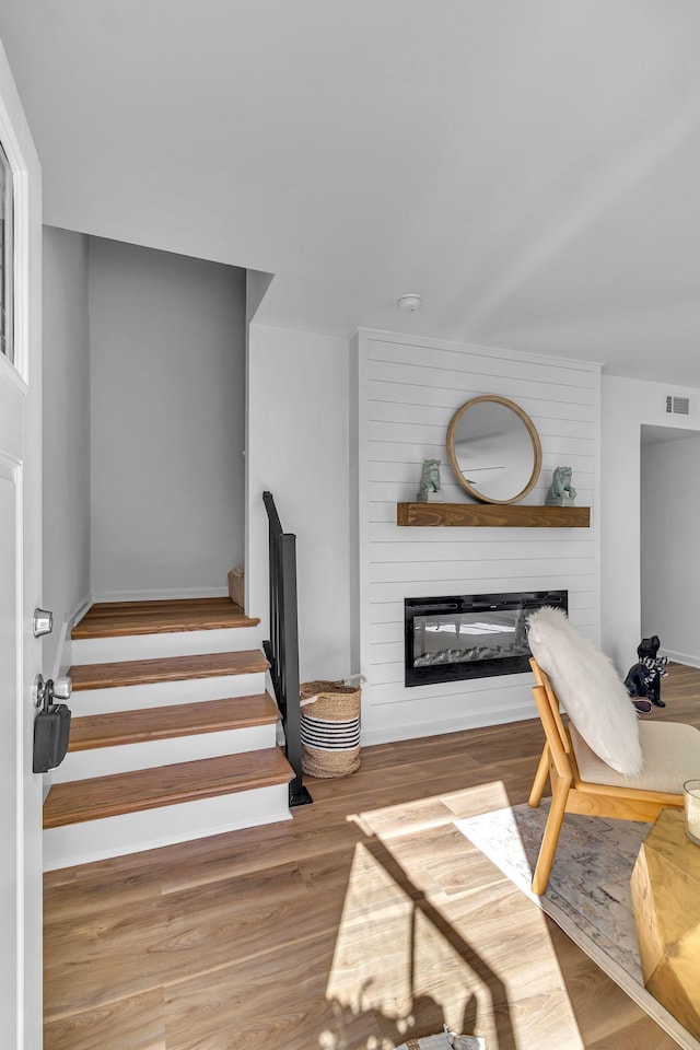 living area featuring a large fireplace, stairs, visible vents, and wood finished floors