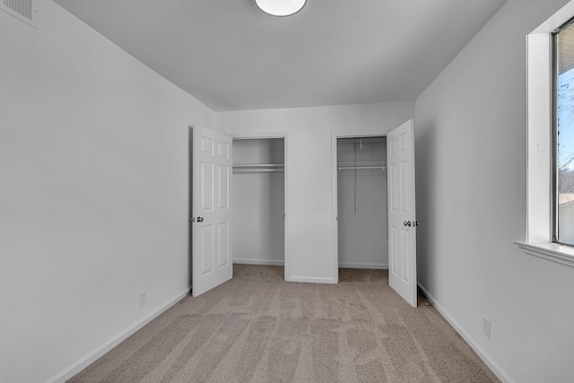 unfurnished bedroom with multiple closets, carpet, visible vents, and baseboards