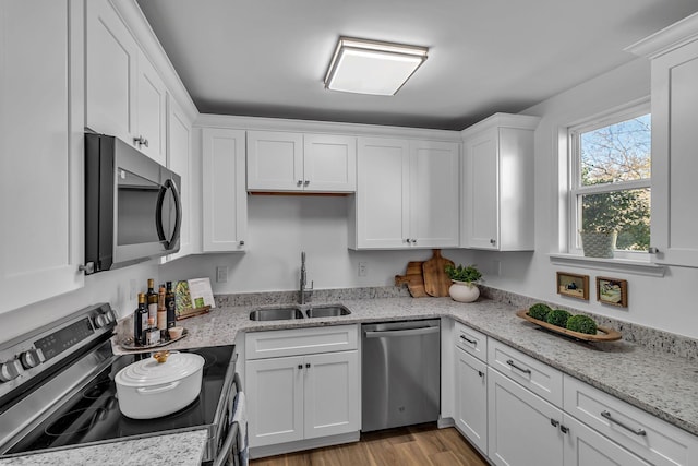 kitchen with white cabinets, light wood-style flooring, stainless steel appliances, and a sink