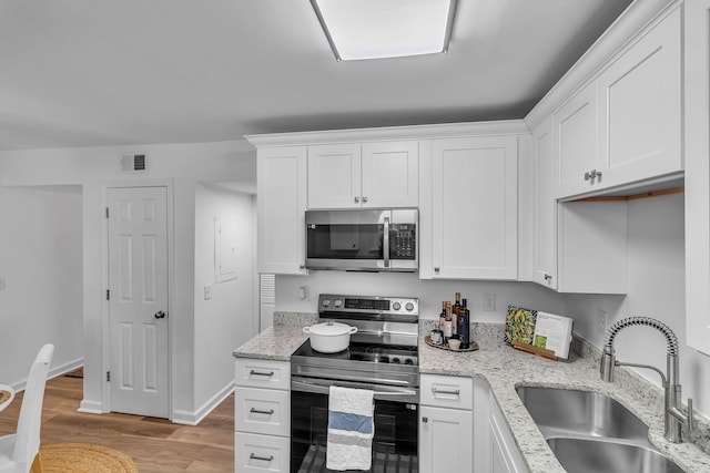 kitchen featuring stainless steel appliances, wood finished floors, a sink, and white cabinetry