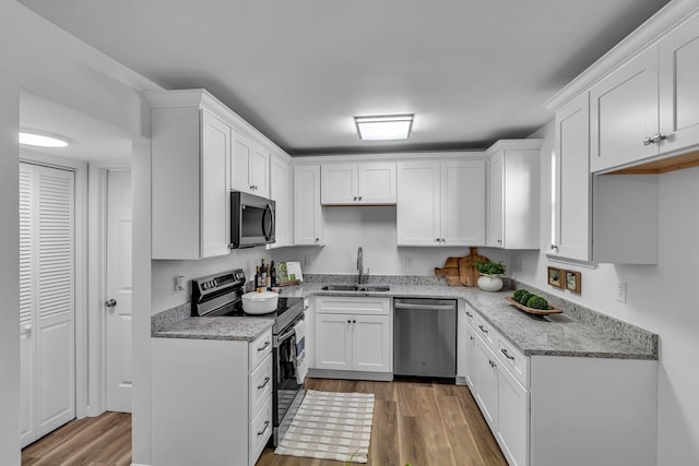 kitchen with stainless steel appliances, light wood finished floors, a sink, and white cabinetry