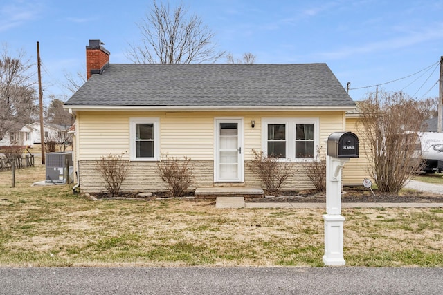 bungalow with central air condition unit, a chimney, a front lawn, and roof with shingles