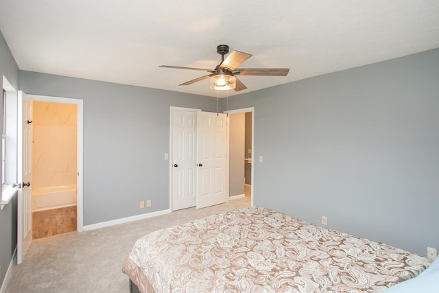 bedroom featuring a closet, light colored carpet, ceiling fan, ensuite bath, and baseboards