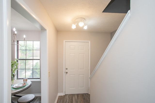 doorway with a textured ceiling, wood finished floors, and baseboards