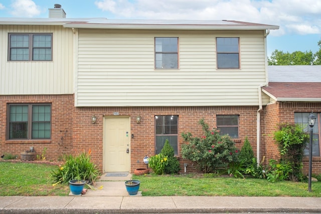 view of front of property with brick siding, a chimney, and a front lawn