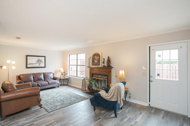 living room with wood finished floors, a fireplace with flush hearth, visible vents, baseboards, and crown molding