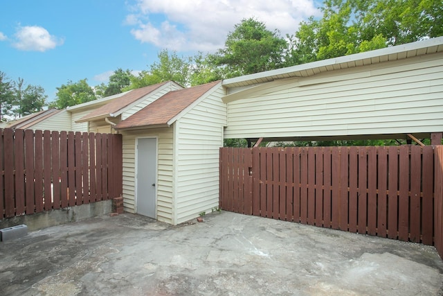 view of property exterior featuring an outbuilding, a shingled roof, fence, a storage unit, and a patio area