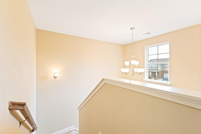 hall with baseboards, visible vents, a chandelier, and an upstairs landing