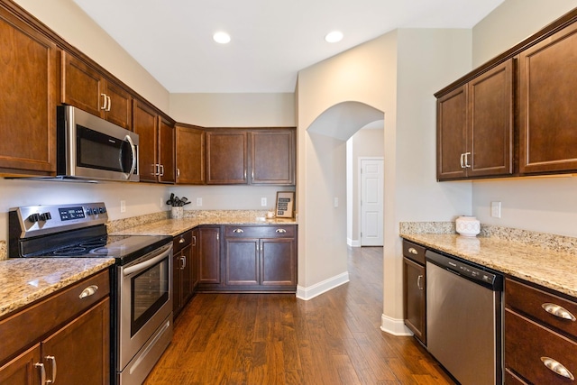 kitchen featuring stainless steel appliances, arched walkways, dark wood-type flooring, and light stone counters