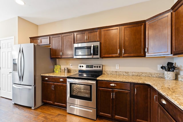 kitchen with dark brown cabinetry, light stone countertops, stainless steel appliances, and wood finished floors