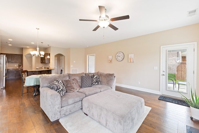 living area with arched walkways, ceiling fan with notable chandelier, dark wood-style flooring, visible vents, and baseboards