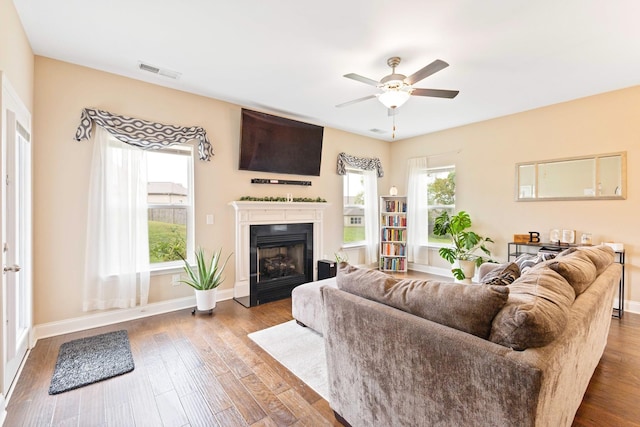 living room featuring baseboards, a fireplace with flush hearth, visible vents, and wood finished floors