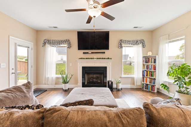 living room featuring visible vents, a fireplace, baseboards, and wood finished floors