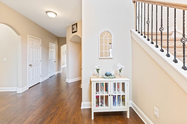 corridor with arched walkways, stairway, wood finished floors, and baseboards