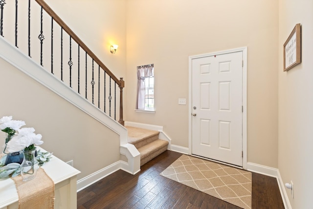 foyer with stairs, a high ceiling, dark wood-style flooring, and baseboards