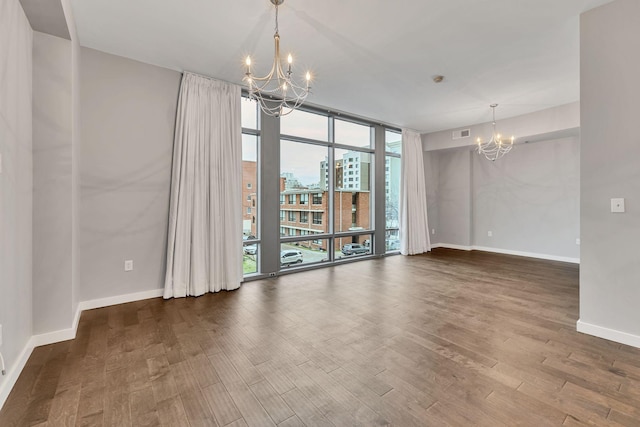 empty room featuring baseboards, floor to ceiling windows, wood finished floors, and an inviting chandelier