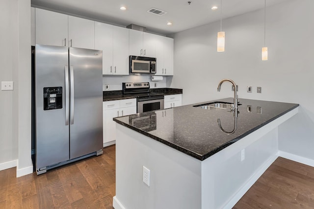 kitchen with a peninsula, a sink, appliances with stainless steel finishes, dark wood-style floors, and decorative light fixtures