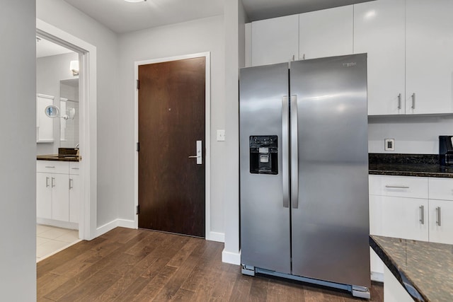 kitchen featuring baseboards, dark wood finished floors, stainless steel fridge with ice dispenser, dark stone countertops, and white cabinetry