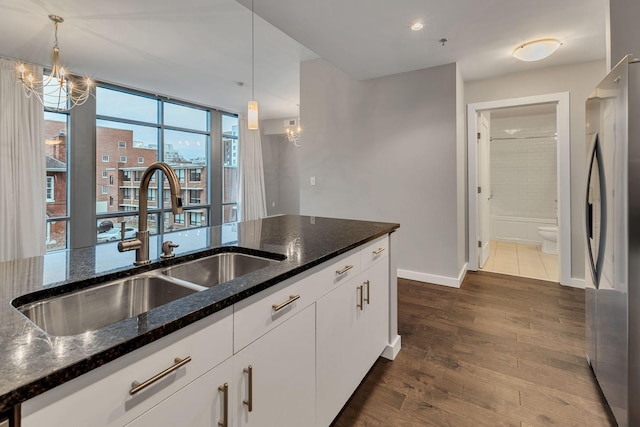 kitchen with dark wood-style flooring, a sink, freestanding refrigerator, dark stone counters, and an inviting chandelier