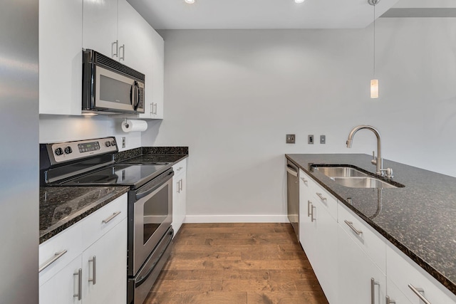 kitchen featuring dark wood-style flooring, stainless steel appliances, hanging light fixtures, a sink, and dark stone countertops