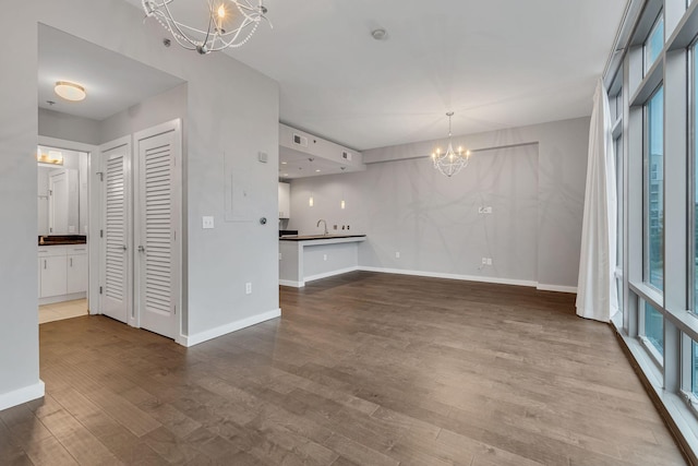 unfurnished living room with baseboards, a notable chandelier, a sink, and wood finished floors