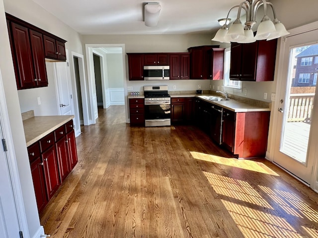 kitchen with reddish brown cabinets, appliances with stainless steel finishes, dark wood-style flooring, light countertops, and a sink