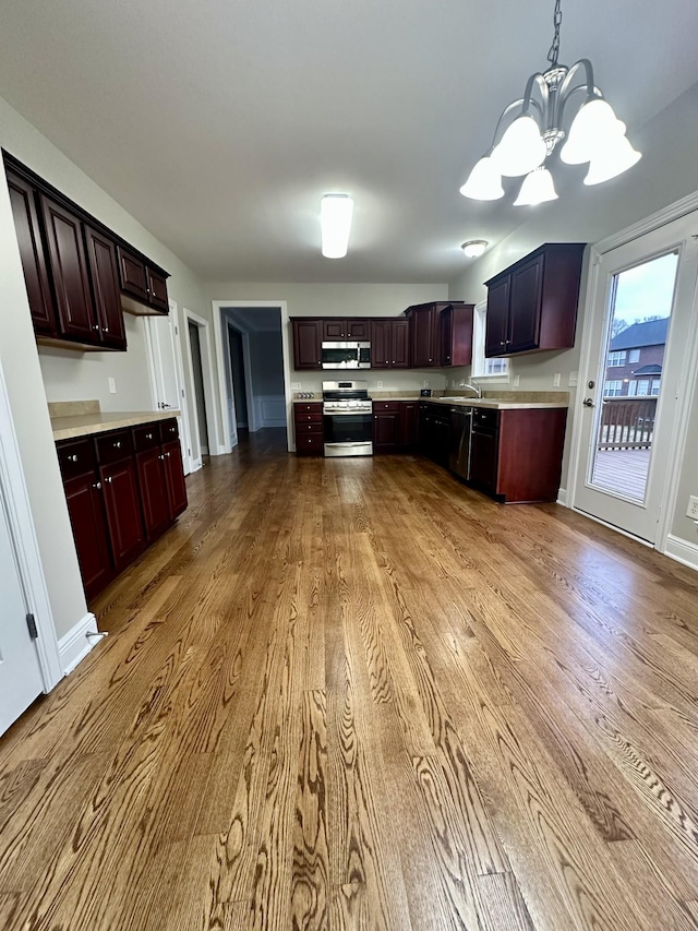 kitchen with wood finished floors, hanging light fixtures, stainless steel appliances, light countertops, and a notable chandelier