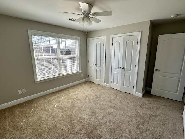 unfurnished bedroom featuring baseboards, visible vents, a ceiling fan, carpet floors, and two closets