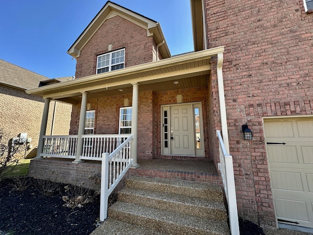 property entrance featuring a porch, brick siding, and an attached garage