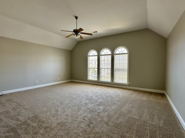 carpeted spare room with vaulted ceiling, baseboards, visible vents, and a ceiling fan