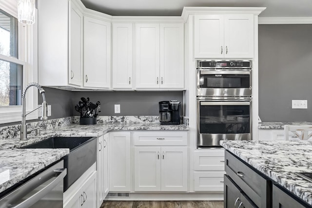 kitchen with ornamental molding, appliances with stainless steel finishes, light stone countertops, and white cabinets