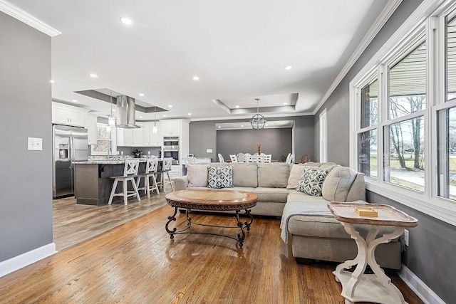 living area featuring light wood-style floors, a raised ceiling, crown molding, and baseboards