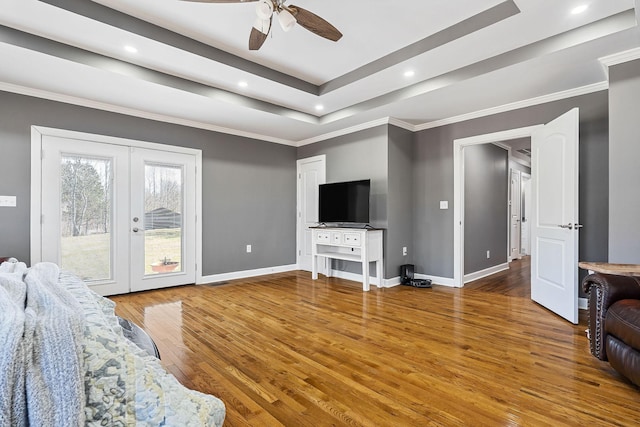 living area with wood finished floors, french doors, a raised ceiling, and baseboards