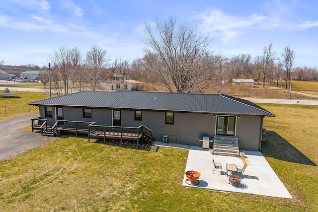 back of property featuring metal roof, a fire pit, french doors, a lawn, and a patio area