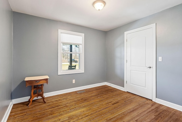 empty room with wood finished floors, visible vents, and baseboards