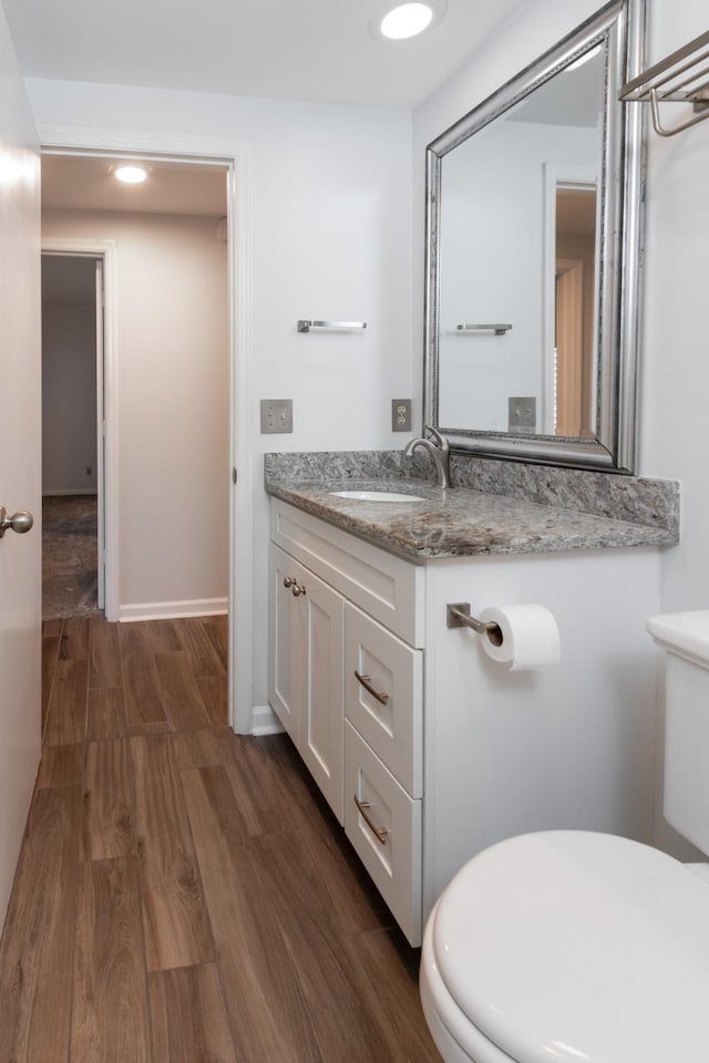 half bath featuring baseboards, toilet, wood finished floors, vanity, and recessed lighting