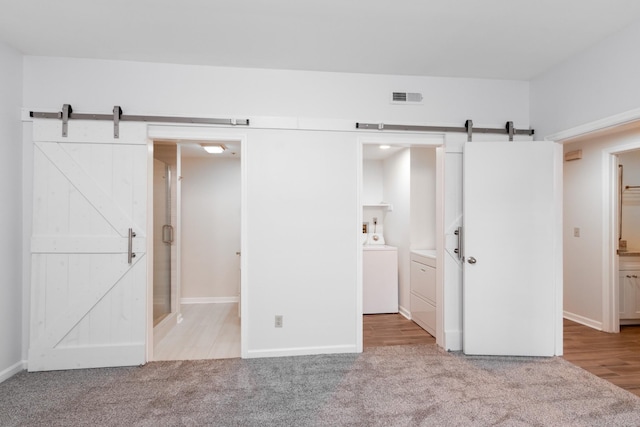 interior space with a barn door, connected bathroom, light carpet, visible vents, and washing machine and clothes dryer