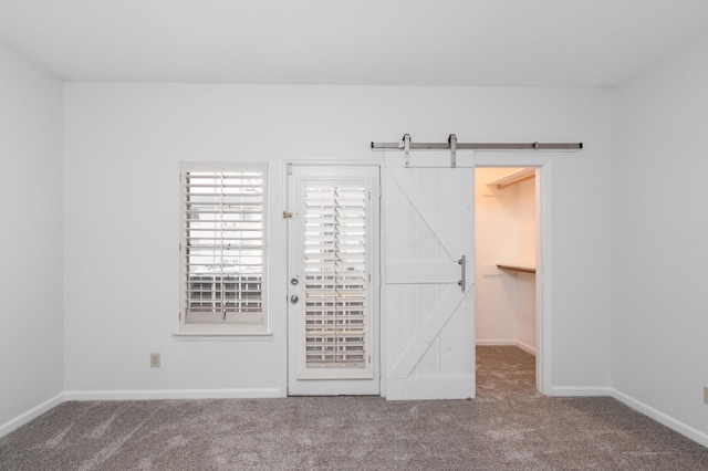 carpeted empty room with a barn door and baseboards