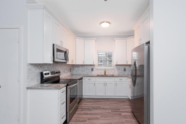 kitchen featuring tasteful backsplash, white cabinets, wood tiled floor, stainless steel appliances, and a sink