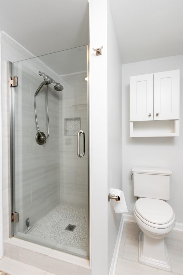 bathroom featuring toilet, a stall shower, tile patterned flooring, and baseboards