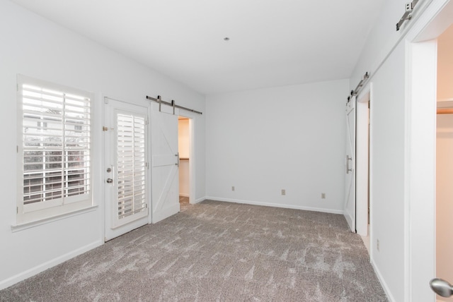 unfurnished bedroom featuring access to exterior, a barn door, carpet flooring, and baseboards