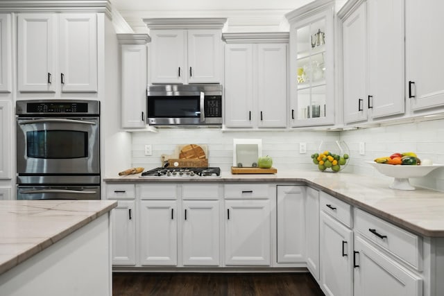 kitchen featuring white cabinets, glass insert cabinets, light stone countertops, stainless steel appliances, and backsplash