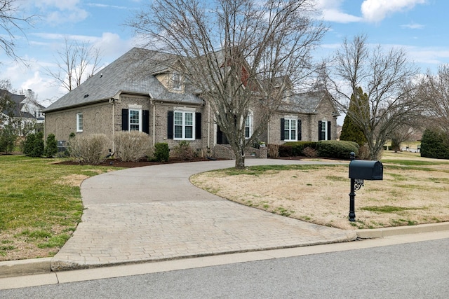 view of front of home featuring a shingled roof, a front lawn, decorative driveway, and brick siding