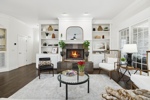 living area with baseboards, a tiled fireplace, dark wood-style floors, crown molding, and built in shelves