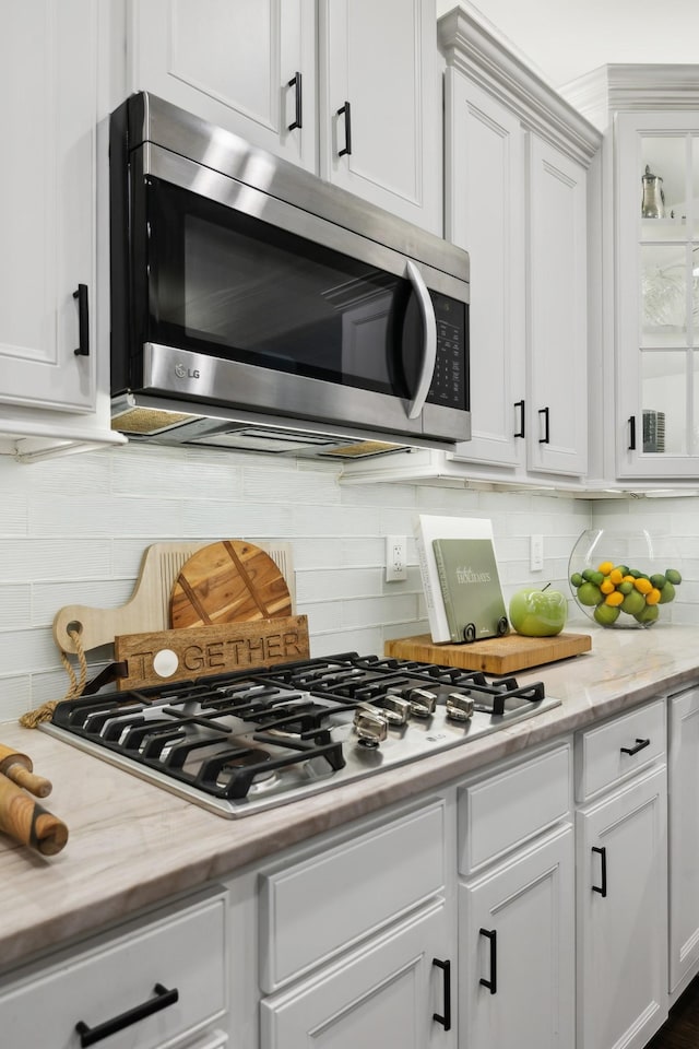 kitchen featuring stainless steel appliances, white cabinetry, glass insert cabinets, and tasteful backsplash