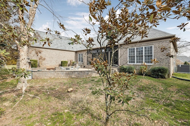 rear view of house with brick siding, a patio, central AC, and a yard