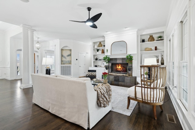 living room featuring built in features, a tile fireplace, visible vents, and ornate columns