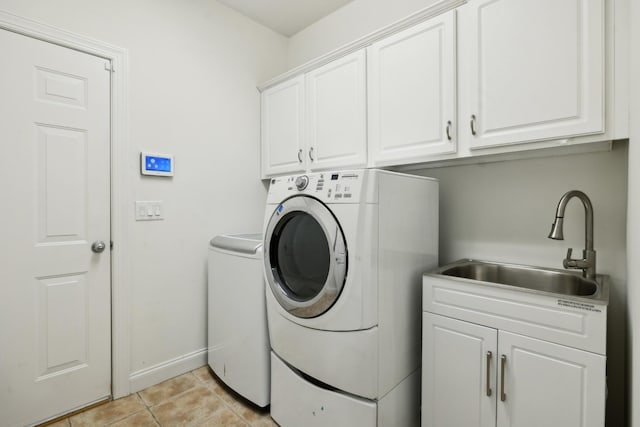 washroom with cabinet space, light tile patterned floors, baseboards, washing machine and dryer, and a sink