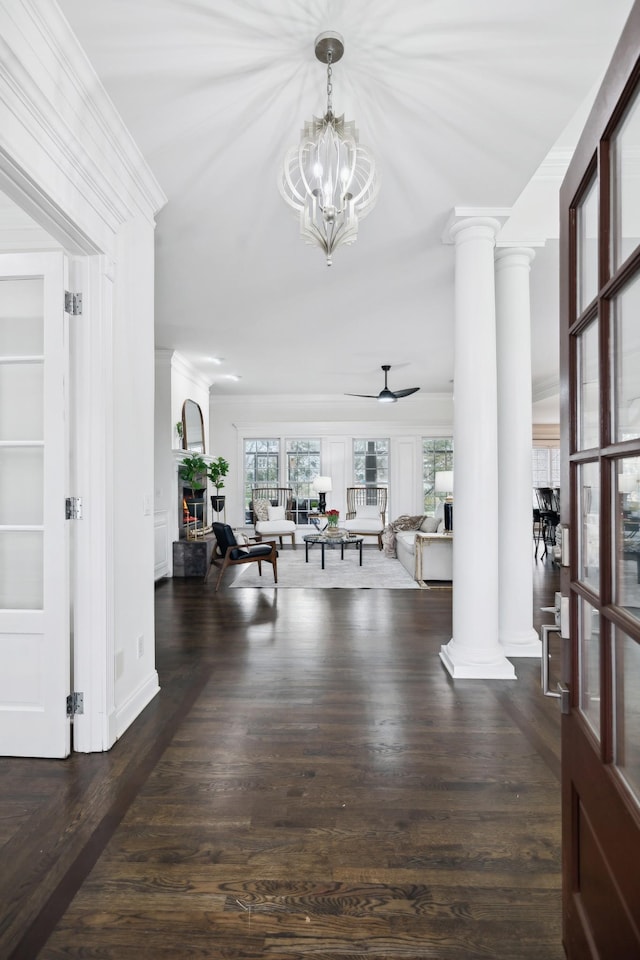 foyer featuring a warm lit fireplace, decorative columns, ceiling fan, wood finished floors, and crown molding